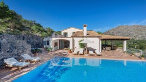 A villa with a swimming pool, outdoor seating, and a mountainous backdrop.