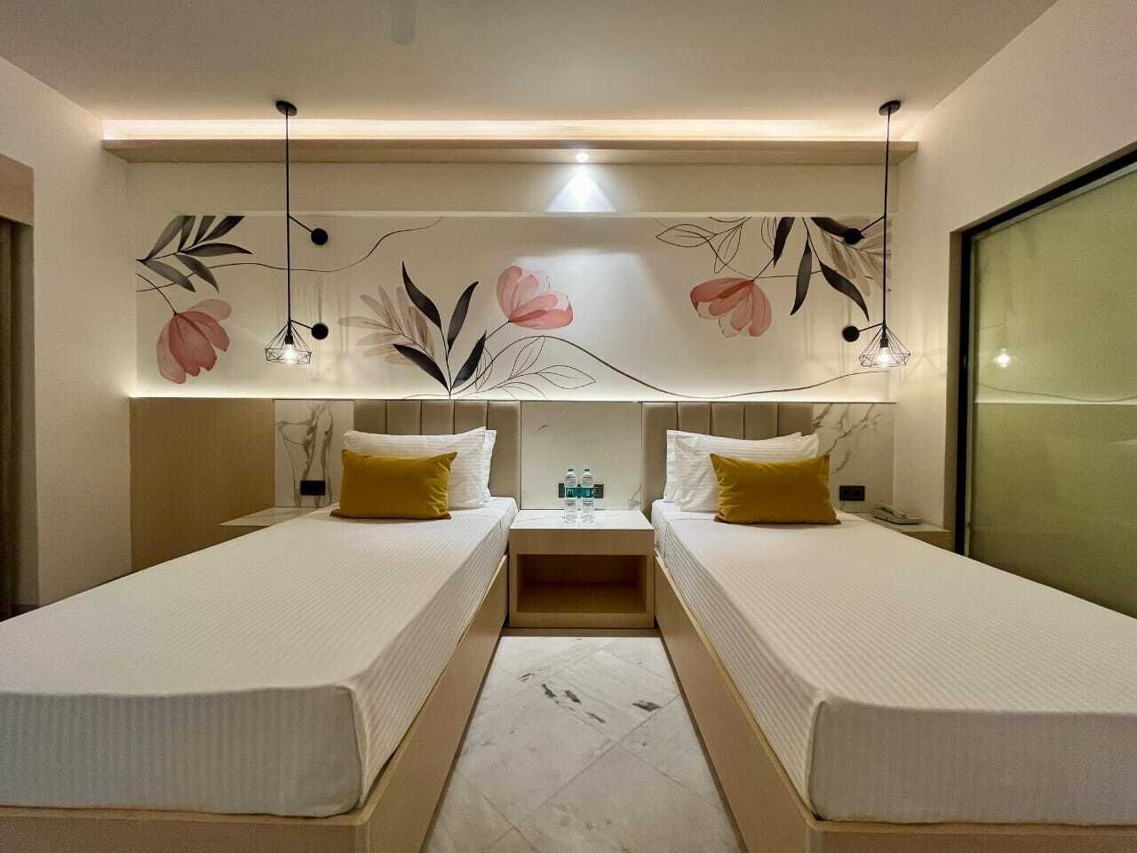 A hotel room with two beds, a nightstand, a wall-mounted light fixture, and a large window.