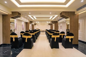 Un salón de conferencias de hotel con filas de sillas negras con cintas doradas, suelo de mármol y un diseño de techo moderno con iluminación empotrada.