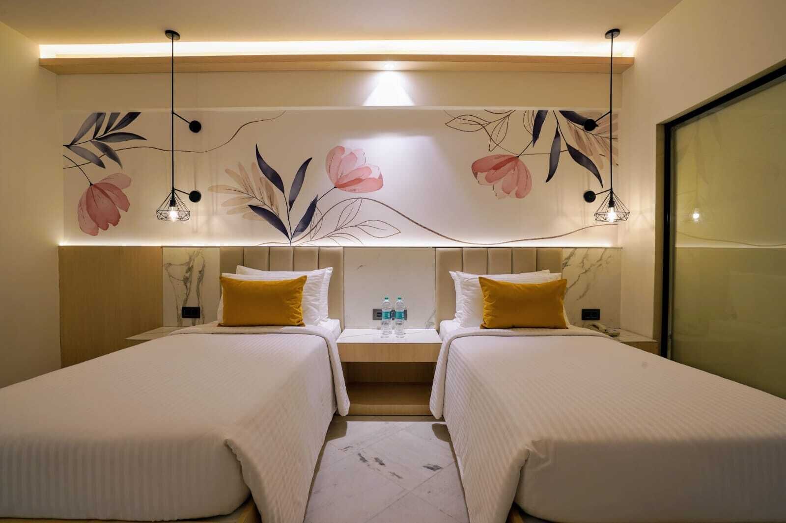 A hotel room with two beds, a nightstand, a water bottle, and a decorative wall with floral patterns.