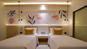 Una camera d'albergo con due letti, un comodino, una bottiglia d'acqua e una parete decorata con motivi floreali.