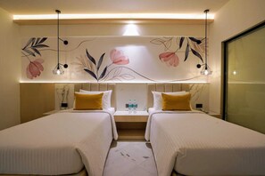 Habitación de hotel con dos camas, una mesita de noche, una botella de agua y un adorno de pared con motivos florales.