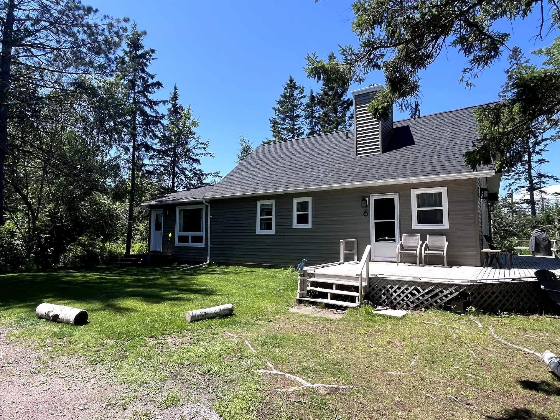 A single-story house with a deck, a chimney, and a small porch with chairs.