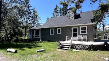 A single-story house with a deck, a chimney, and a small porch with chairs.
