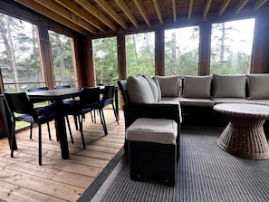 A covered outdoor seating area with a table and chairs, a sofa with cushions, and a wicker coffee table.