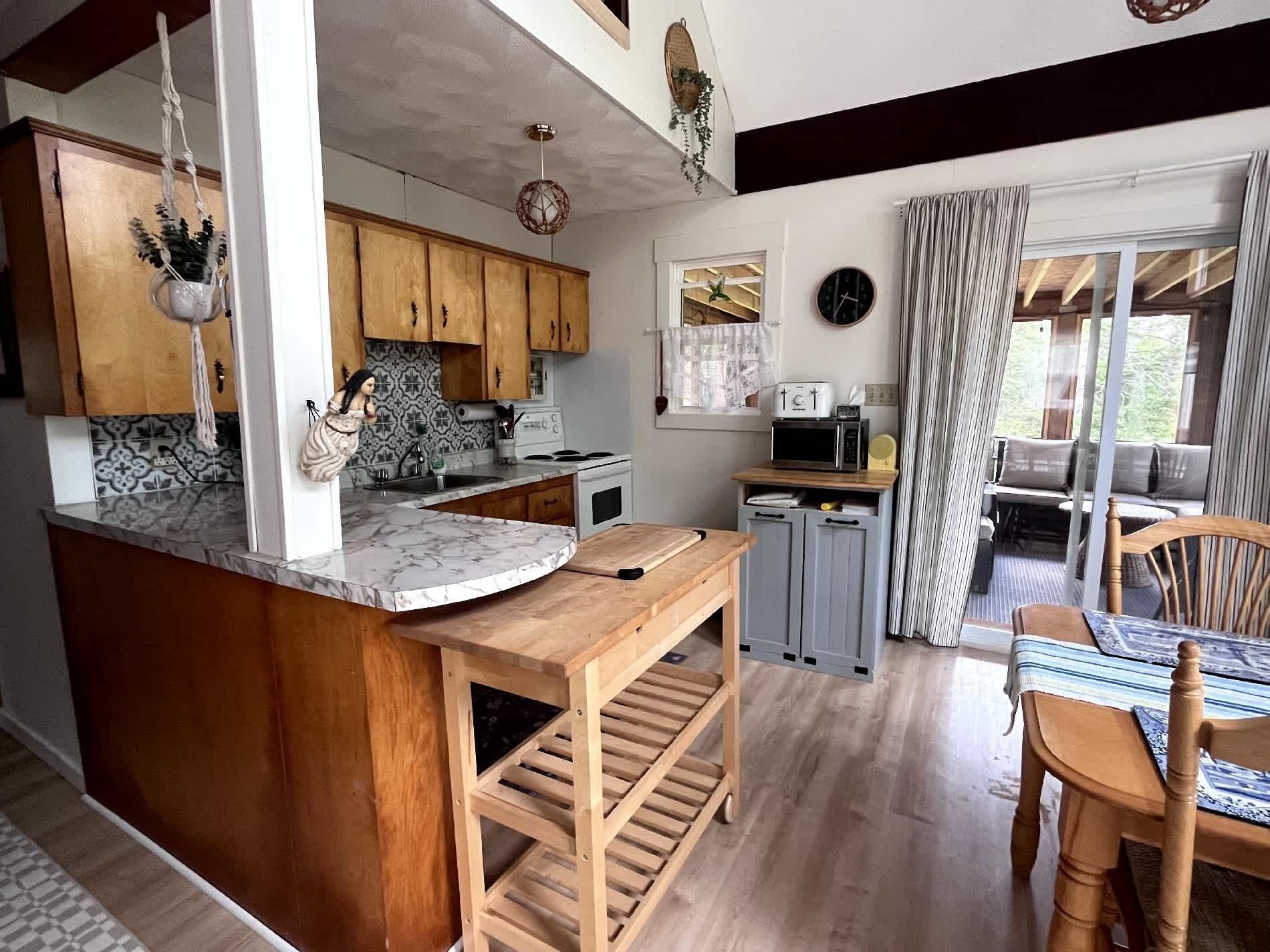 Una cocina con armarios de madera, encimera de mármol, un fregadero, estufa y un comedor con mesa y sillas.