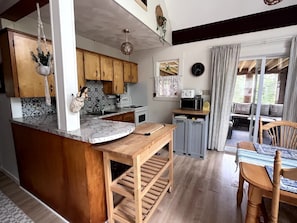 A kitchen with wooden cabinets, a marble countertop, a sink, a stove, and a dining area with a table and chairs.