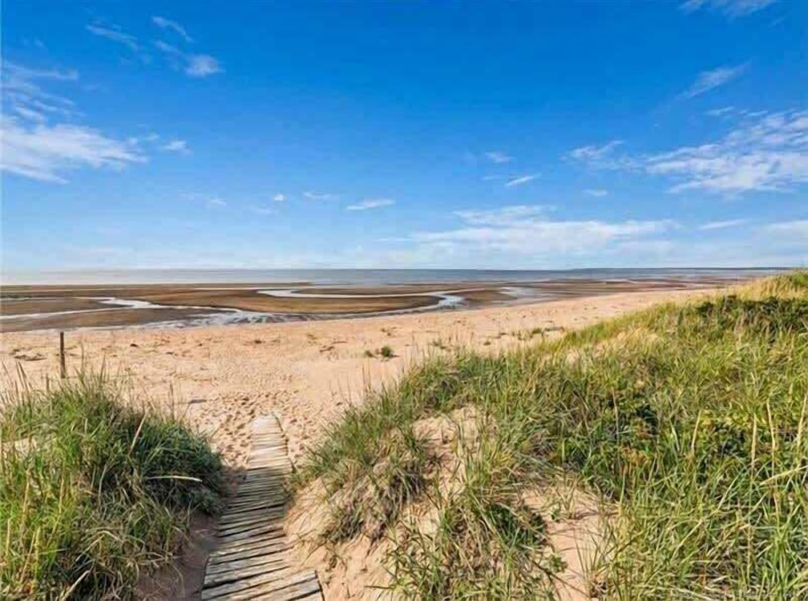 Ein sandiger Strand mit einem hölzernen Promenadenweg, der zum Wasser führt, unter blauem Himmel.