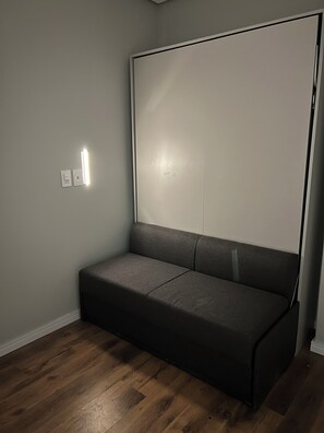A room with a dark grey sofa, a white wall, and a wooden floor. - Loft4 Brooklin Berrini Vila Olímpia Airport CGH (São Paulo)
