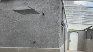 Ein überdachter Außenbereich mit einer grauen, strukturierten Wand, einer Metalttür und einem gefliesten Boden.