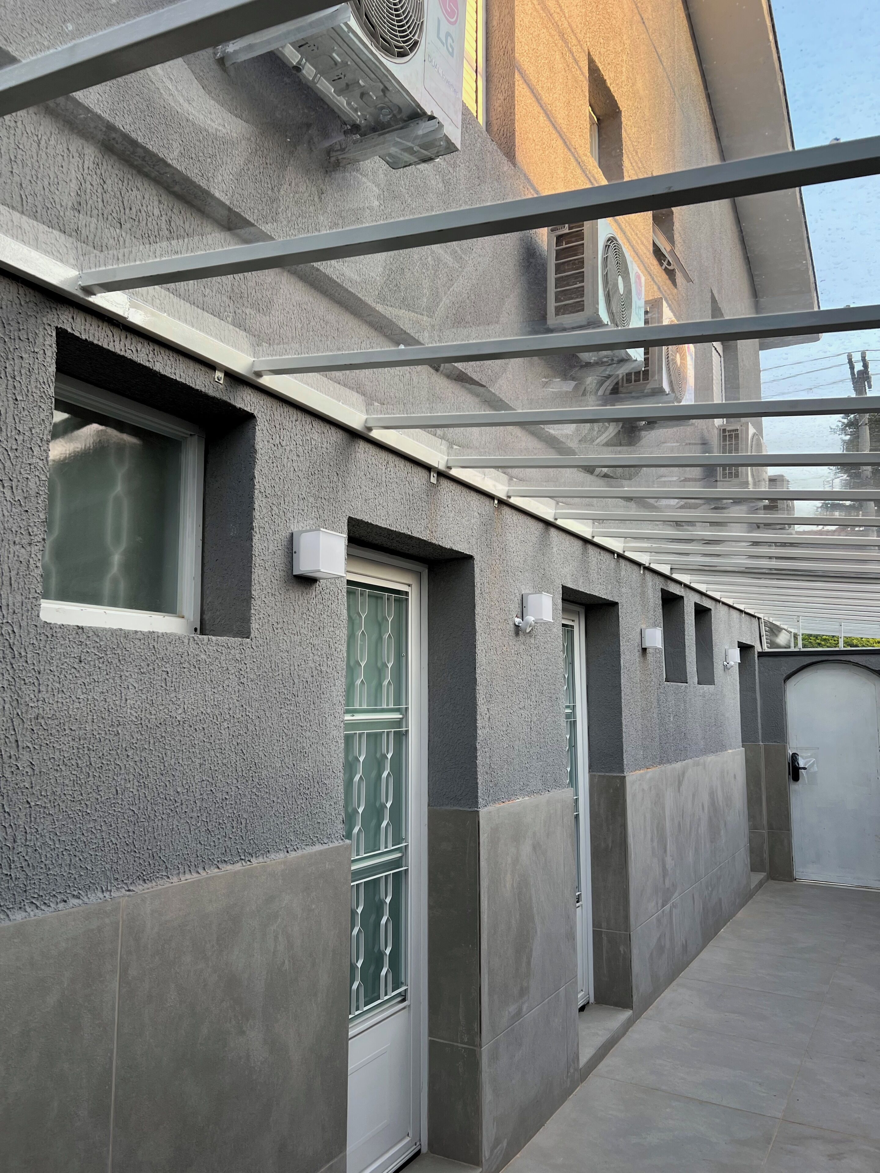 A covered outdoor area with a metal roof, a building with textured walls, and a door with a metal grille.