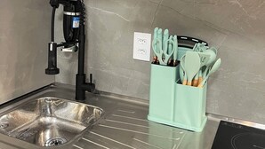 Eine Küche mit einem modernen Waschbecken, einem schwarzen Wasserhahn und einem türkisblauen Zubehörbehälter.