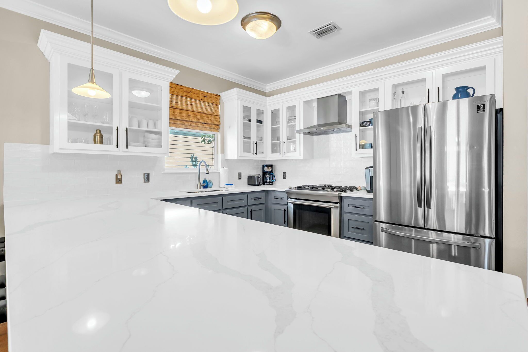 A modern kitchen with white cabinetry, a stainless steel refrigerator, and a marble countertop.