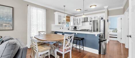 A modern kitchen with white cabinets, stainless steel appliances, and a wooden dining table.