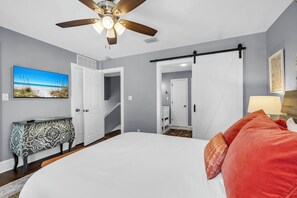 A bedroom with a bed, a ceiling fan, a TV, a console table, and a door leading to a hallway. - Sugar Sand Bungalow with 3 Min Walk to Beach (Santa Rosa Beach)