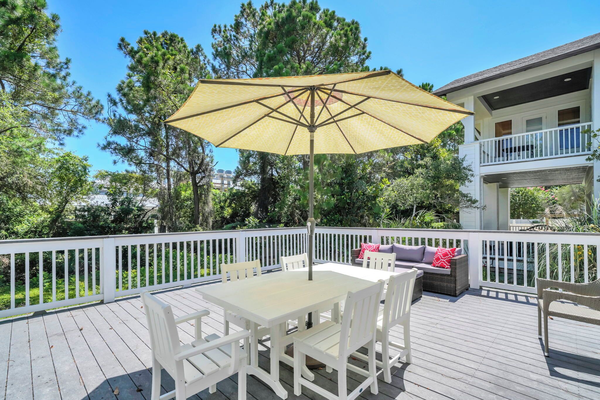 A wooden deck with a table and chairs, a yellow umbrella, and a white railing.