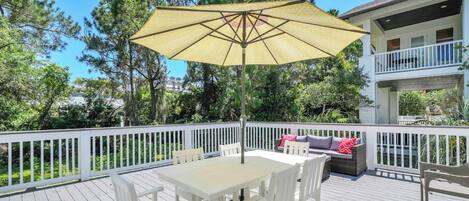 A wooden deck with a table and chairs, a yellow umbrella, and a white railing.