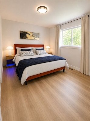 A neatly arranged bedroom with a wooden bed, two bedside tables, a wall-mounted lamp, and a window with curtains.