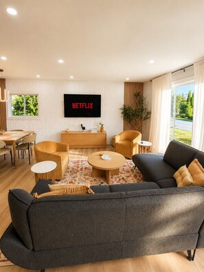 Un salon moderne comprenant un canapé, des fauteuils, une table basse, un téléviseur et un coin repas.