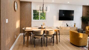 Una sala de estar moderna con comedor, paneles de madera, un televisor de pantalla plana y un sillón amarillo.