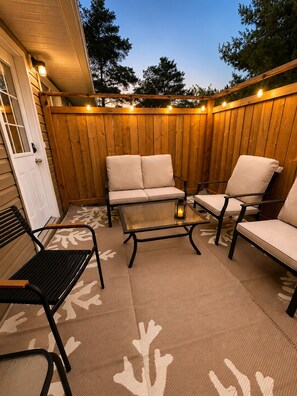 An outdoor patio with a wooden fence, a sofa, two chairs, a small table, and a bench.