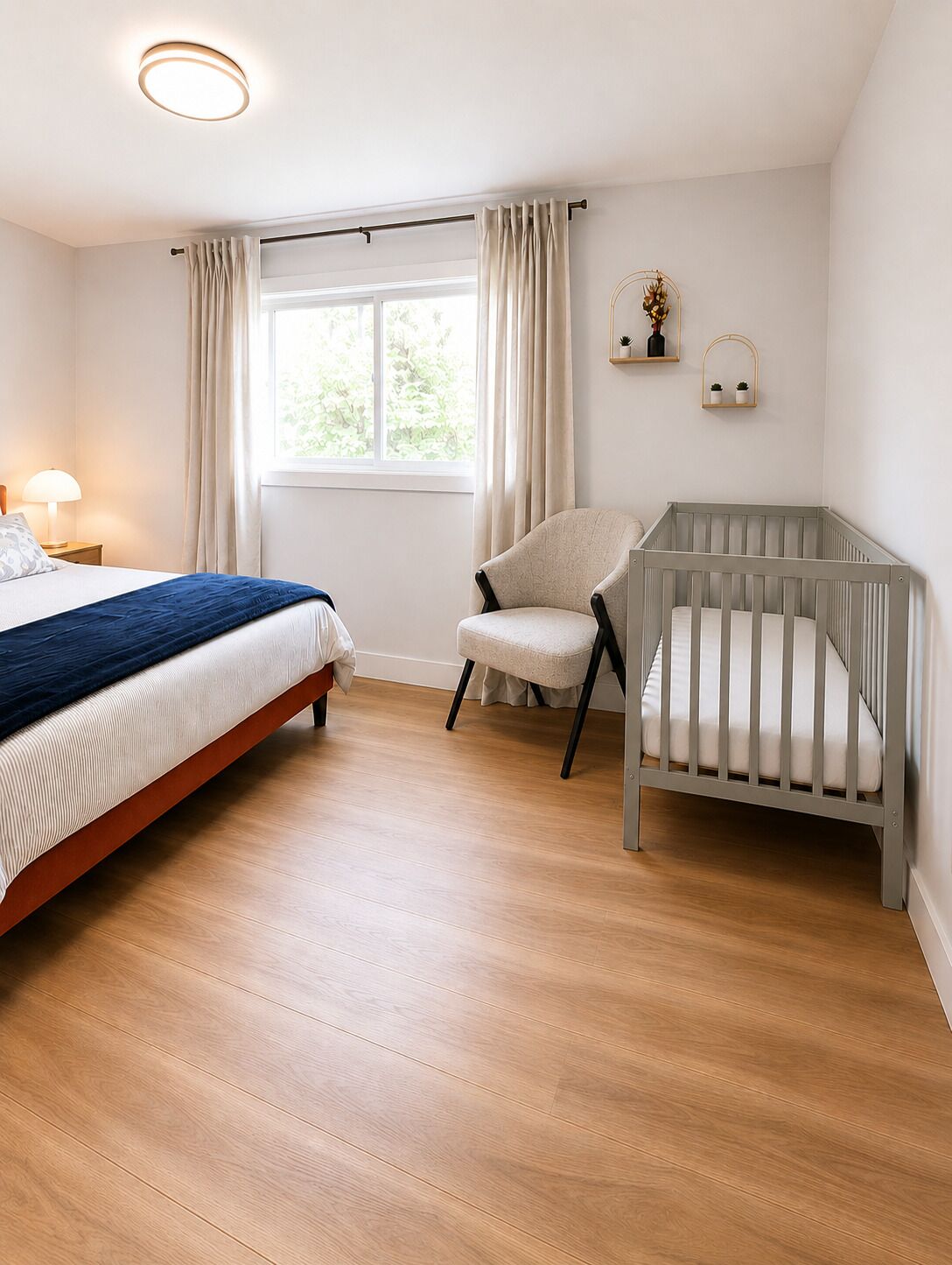Ein Schlafzimmer mit einem Bett, einem Sessel, einem Babybett, einem Fenster und einer Nachttischlampe.