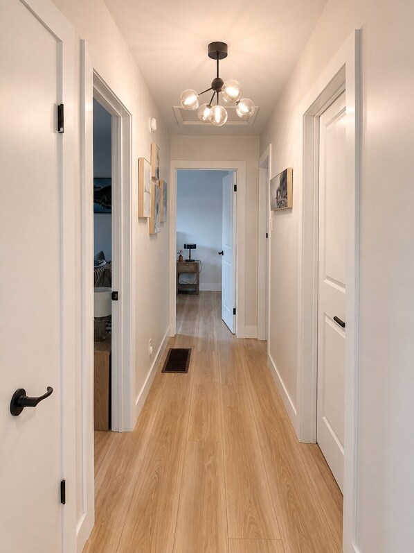A hallway with wooden flooring, white walls, and a ceiling light fixture.