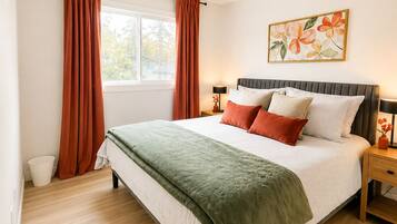 A bedroom with a bed, curtains, a bedside table, a lamp, and a window.