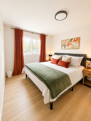 A bedroom with a bed, curtains, a bedside table, a lamp, and a window.