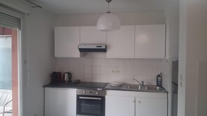 Een kleine keuken met witte kastjes, een inbouwoven, een spoelbak en een hanglamp.