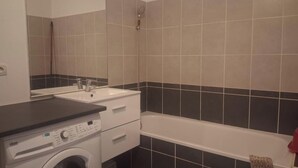 Een badkamer met een wasmachine, een wastafel en een bad.