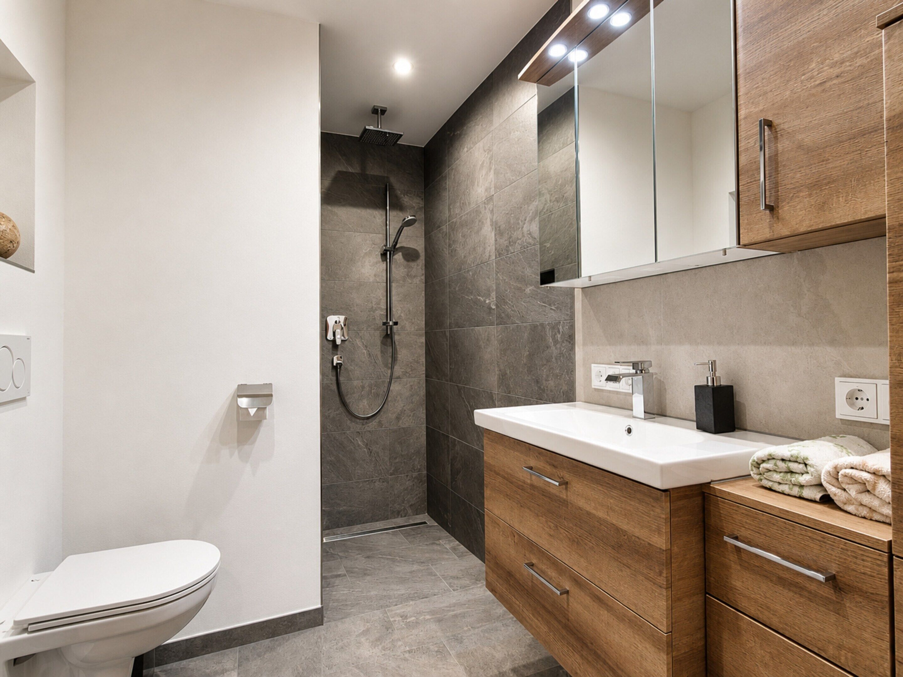 A modern bathroom with a toilet, a shower, and a vanity with drawers and a mirror.