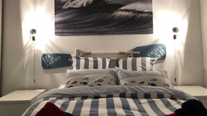 A bedroom with a bed, striped bedding, and a wall-mounted painting of waves. - Elegant apartment close to the port and the market (Saint-Martin-de-Ré)