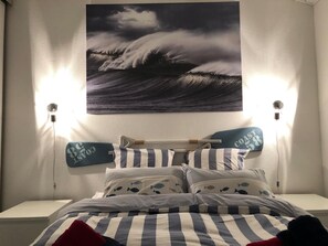 A bedroom with a bed, striped bedding, and a wall-mounted painting of waves. - Elegant apartment close to the port and the market (Saint-Martin-de-Ré)