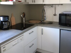 A modern kitchen with a built-in dishwasher, a coffee maker, a microwave, and a sink. - Elegant apartment close to the port and the market (Saint-Martin-de-Ré)
