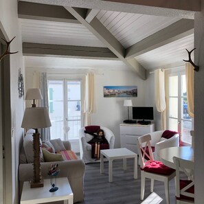A room with a sofa, chairs, a table, a TV, and a window with curtains. - Elegant apartment close to the port and the market (Saint-Martin-de-Ré)