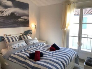 A hotel room with a bed, a painting of waves, a window with curtains, and a view of the outside. - Elegant apartment close to the port and the market (Saint-Martin-de-Ré)
