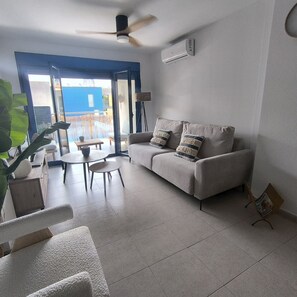 A living room with a sofa, a coffee table, and a chair. There is a ceiling fan and an air conditioning unit. - Puntarró (Peñiscola)