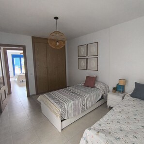 A bedroom with a bed, a nightstand, a lamp, a wardrobe, and a door leading to another room. - Puntarró (Peñiscola)