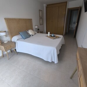 A neatly arranged bedroom with a bed, bedside tables, a wardrobe, and a door leading to another room. - Puntarró (Peñiscola)