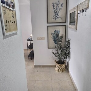 A hallway with framed botanical prints on the wall, a small table with a vase, and a macrame plant pot. - Puntarró (Peñiscola)