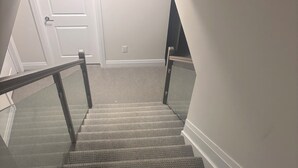 A carpeted staircase with a glass railing, white walls, and a door at the top.