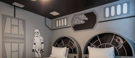 A room with two beds, each with a starry night sky design on the headboard, a wall with a space-themed mural, and a Stormtrooper figure.