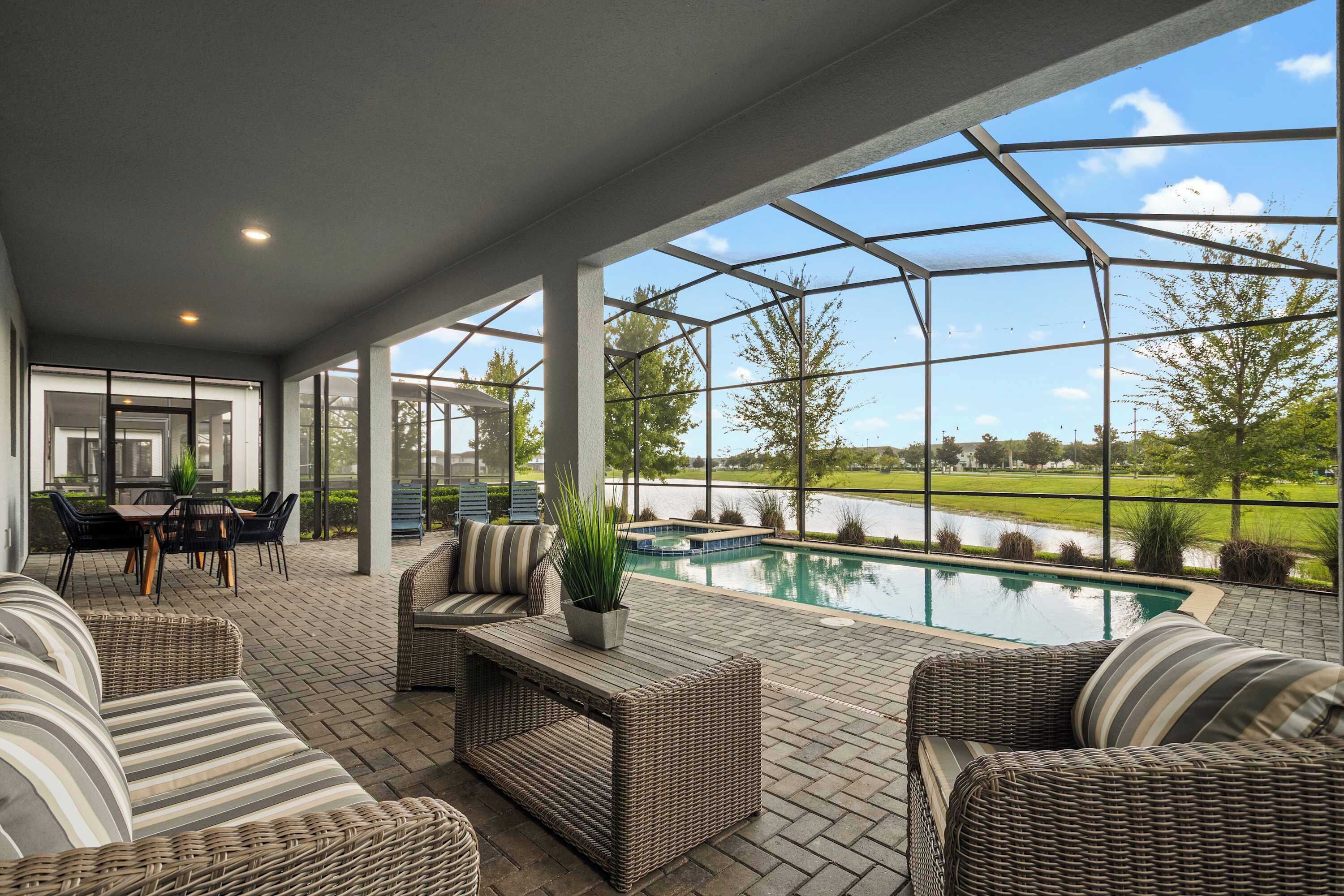 A covered patio area with wicker furniture, a pool, and a view of a lake.