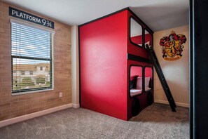 Een kamer met een rode stapelbed, een raam met jaloezieën, een bakstenen muur en een Gryffindor-wapen op de muur.