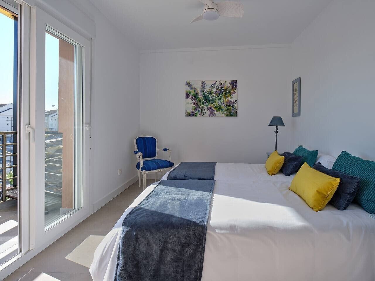 A bedroom with a bed, a chair, a painting, and a view through a sliding door.