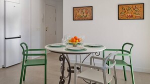 Een eethoek met een ronde tafel, vier stoelen, een koelkast en twee aan de muur hangende schilderijen.
