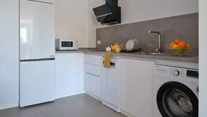 A modern kitchen with white cabinetry, a built-in microwave, a black range hood, and a washing machine. - Ocean View Apartments on Boulevard, Apartame. (San Pedro Alcántara)