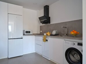 Eine moderne Küche mit weißen Schränken, einer eingebauten Mikrowelle, einer schwarzen Dunstabzugshaube und einer Waschmaschine.