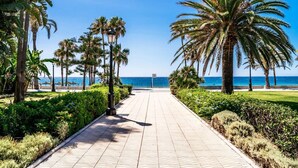 A paved walkway lined with palm trees and greenery, leading to a beach with the ocean in the background. - Ocean View Apartments on Boulevard, Apartame. (San Pedro Alcántara)